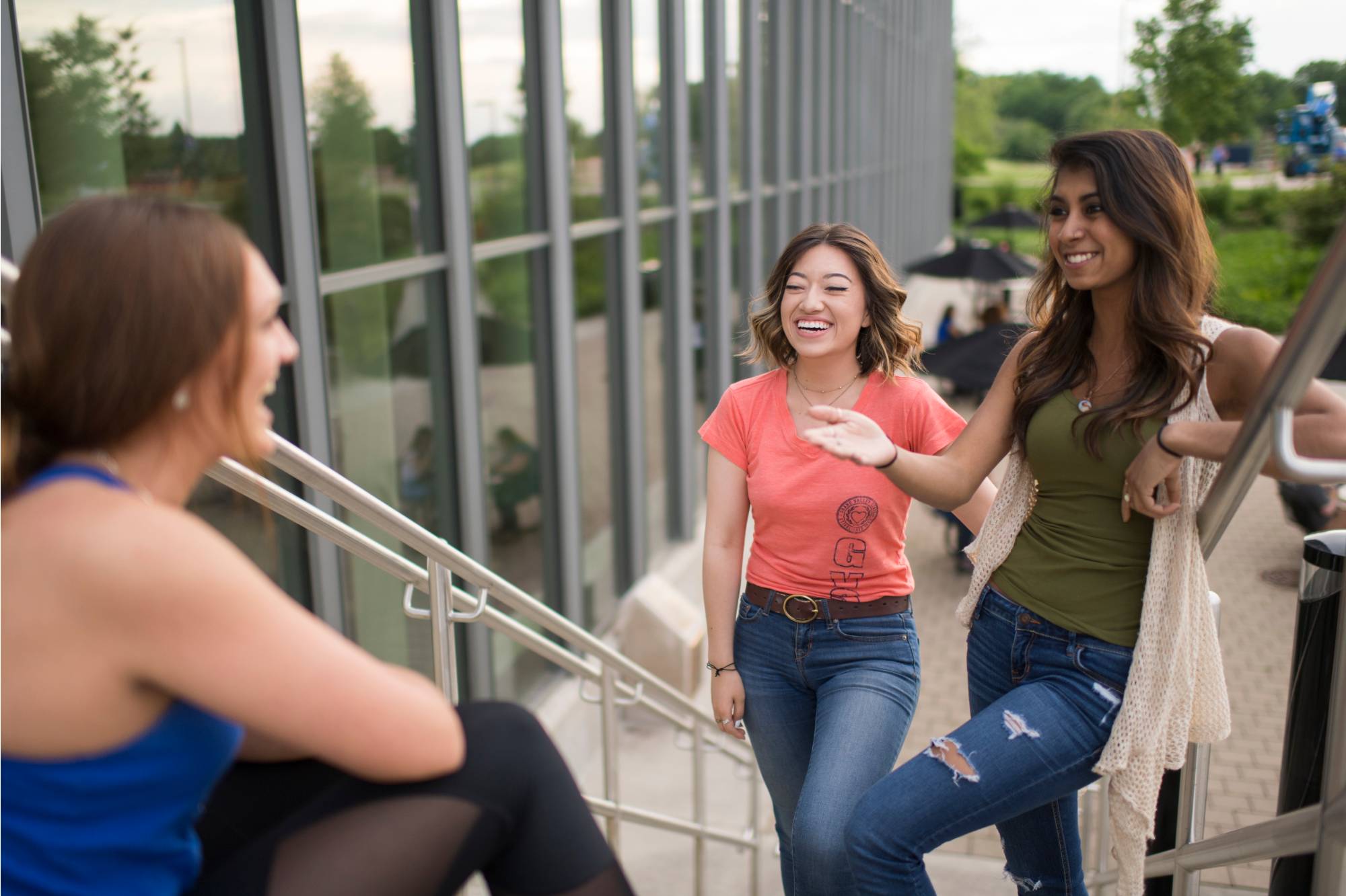 Three students talking while standing on a staircase outside of the Mary Idema Pew Library.